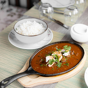 a skillet of etouffee on a table next to a bowl of white rice